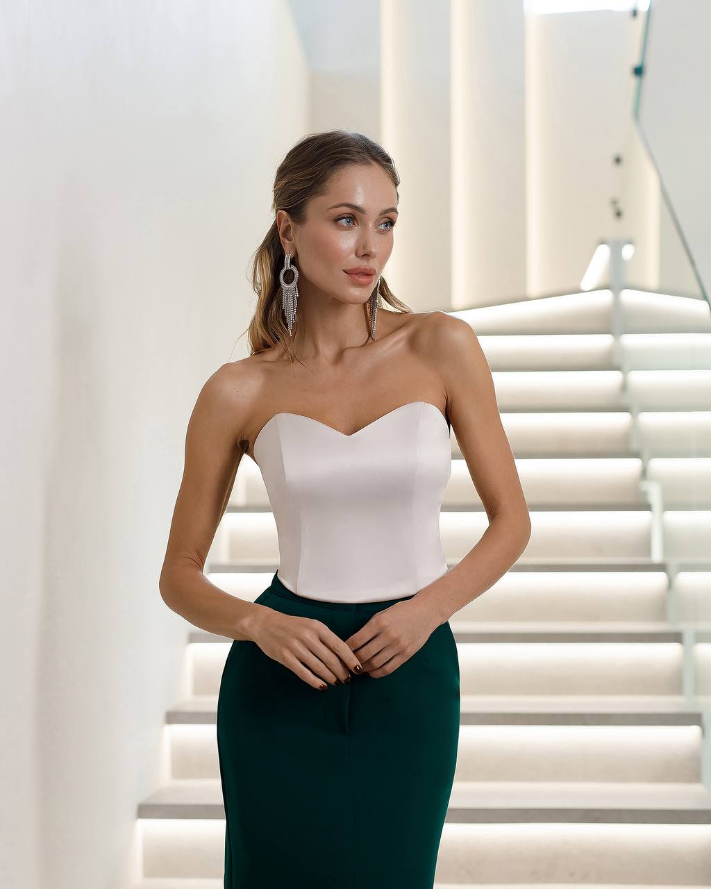 Woman wearing a strapless white top and green pencil skirt in an indoor setting.
