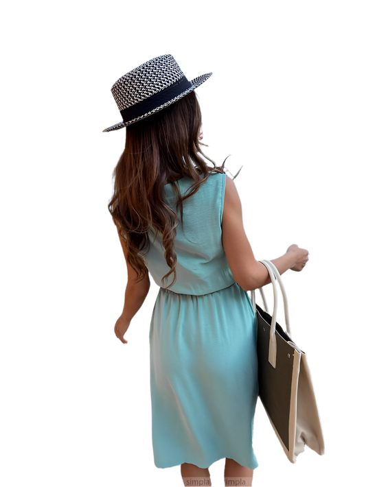 Woman in a light blue dress and black and white hat holding a beige bag on a white background