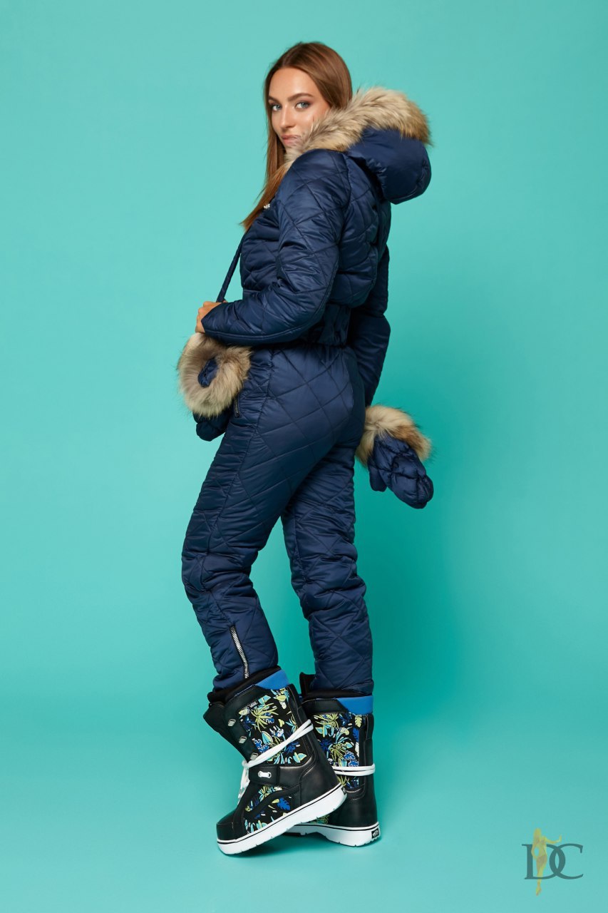 Person wearing a blue winter jumpsuit with fur trim on a teal background