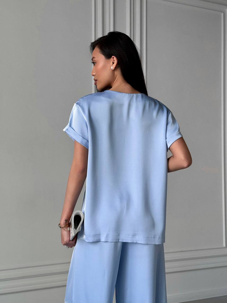 Woman wearing a light blue outfit standing against a gray wall.