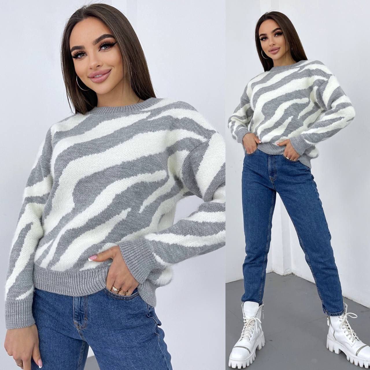 Woman wearing a gray and white zebra pattern sweater with blue jeans and white sneakers on a plain background.