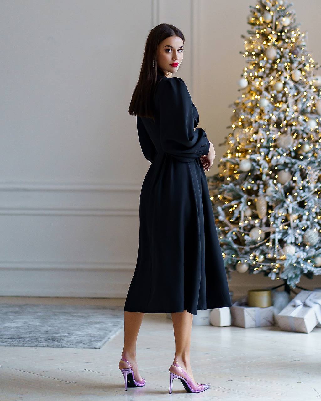 Woman in a black dress standing in a room with a decorated Christmas tree.