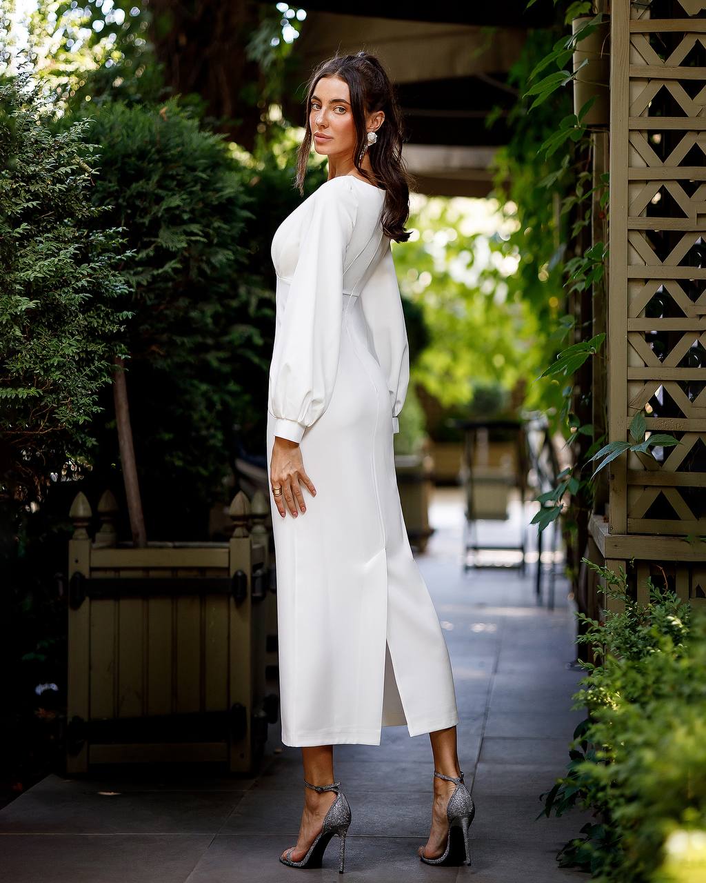 Woman in a white dress standing outdoors with greenery around