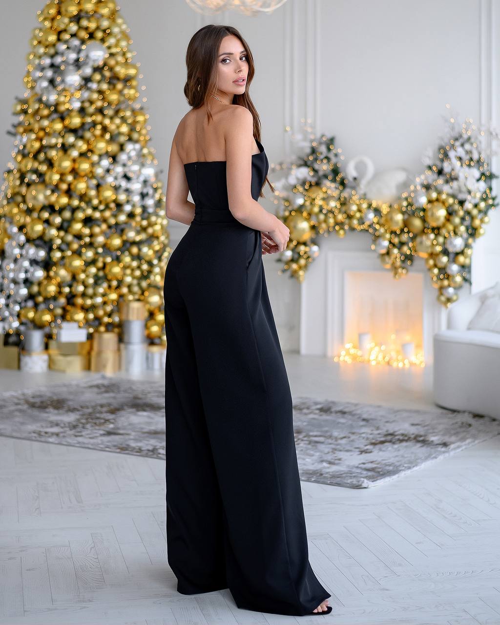 Woman in a black strapless gown standing in a decorated room with Christmas trees.