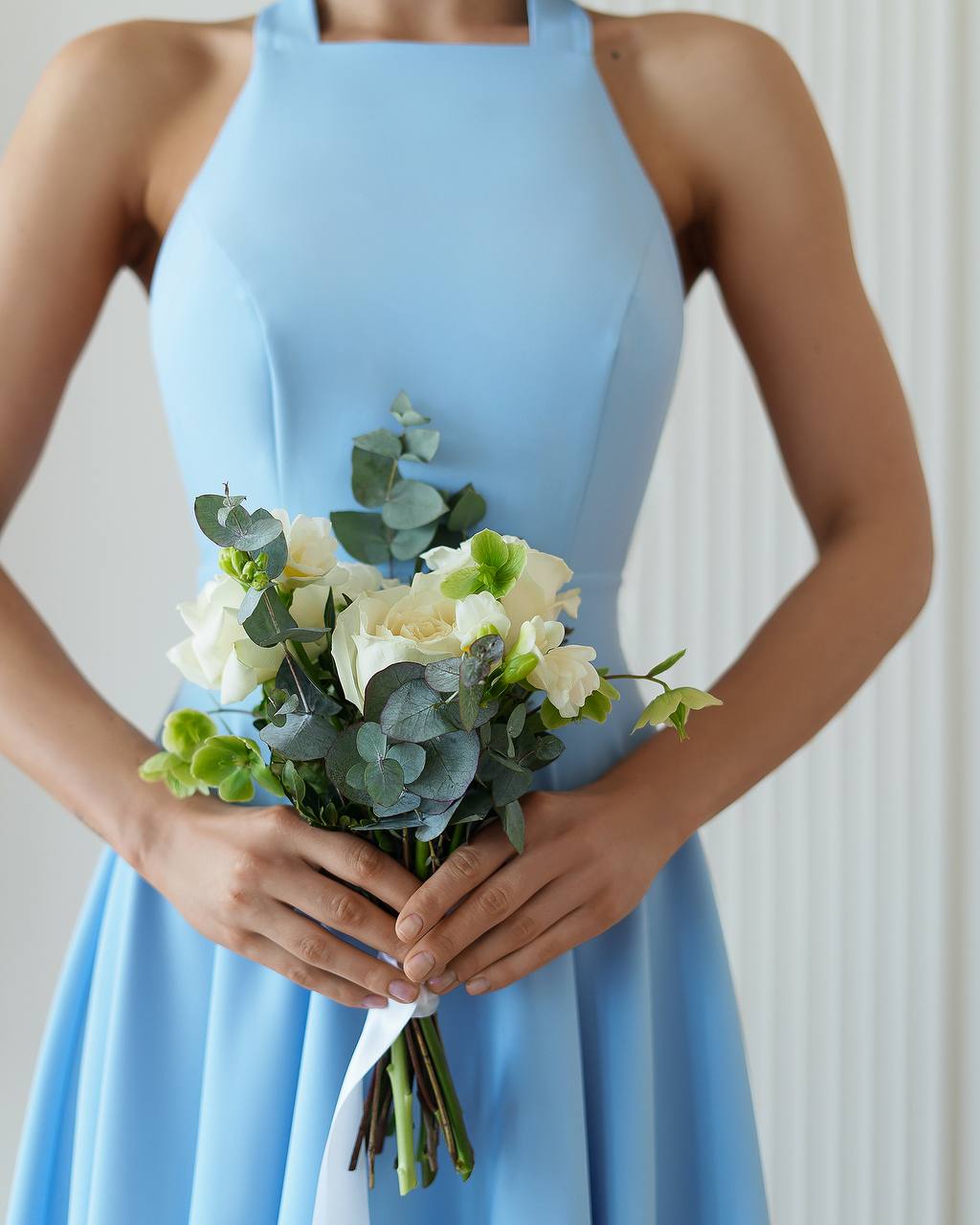 Person wearing a light blue dress holding a bouquet of flowers against a neutral background