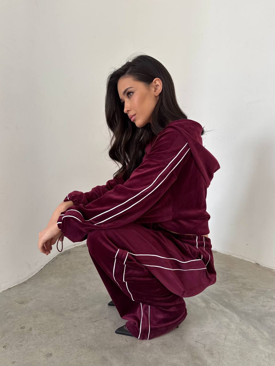 Woman wearing a burgundy tracksuit with white stripes on a plain background