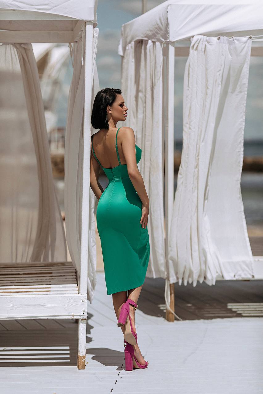 Woman in a green dress standing between white canopies on a bright day.