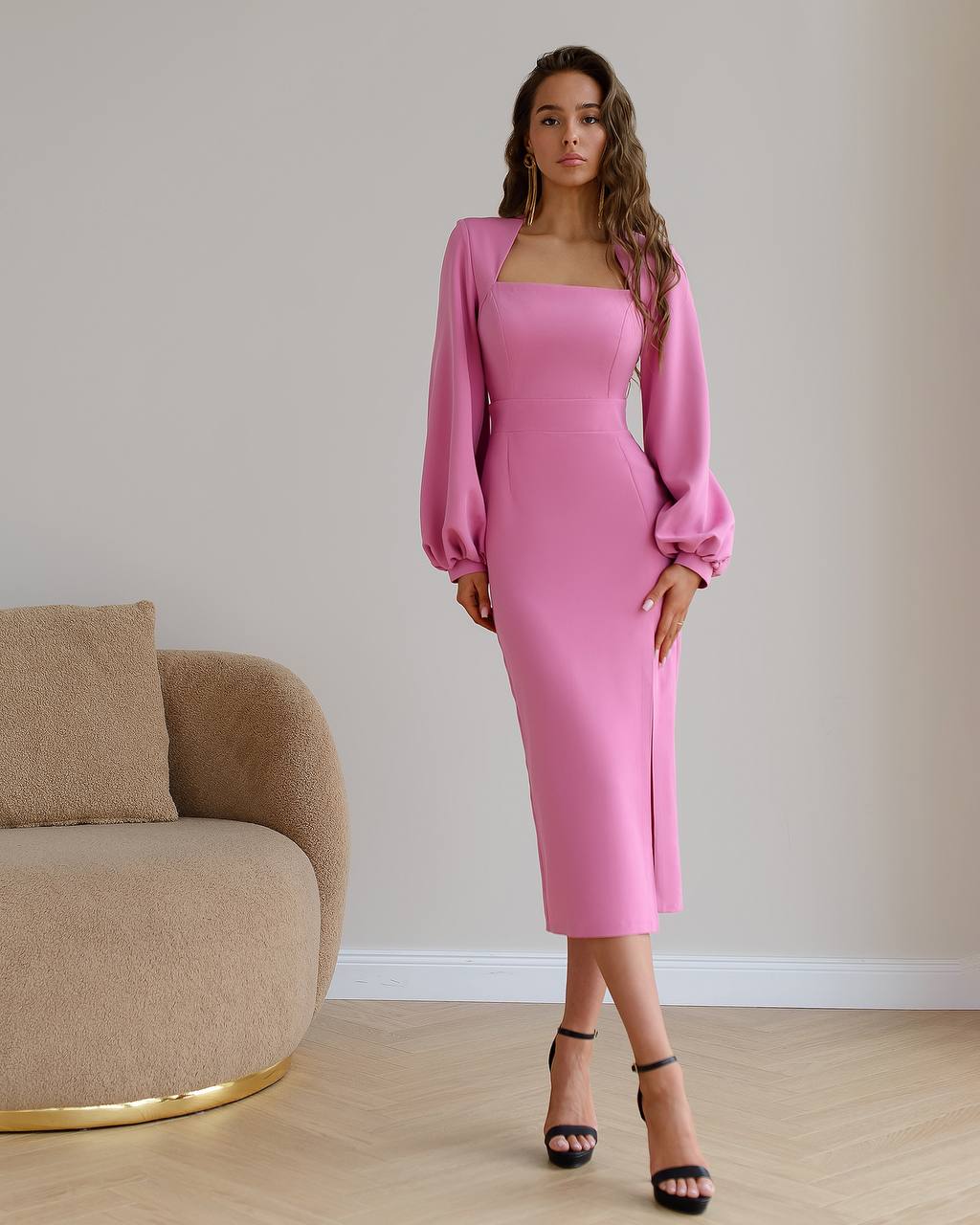 Woman wearing a pink dress standing in a room with a beige armchair.