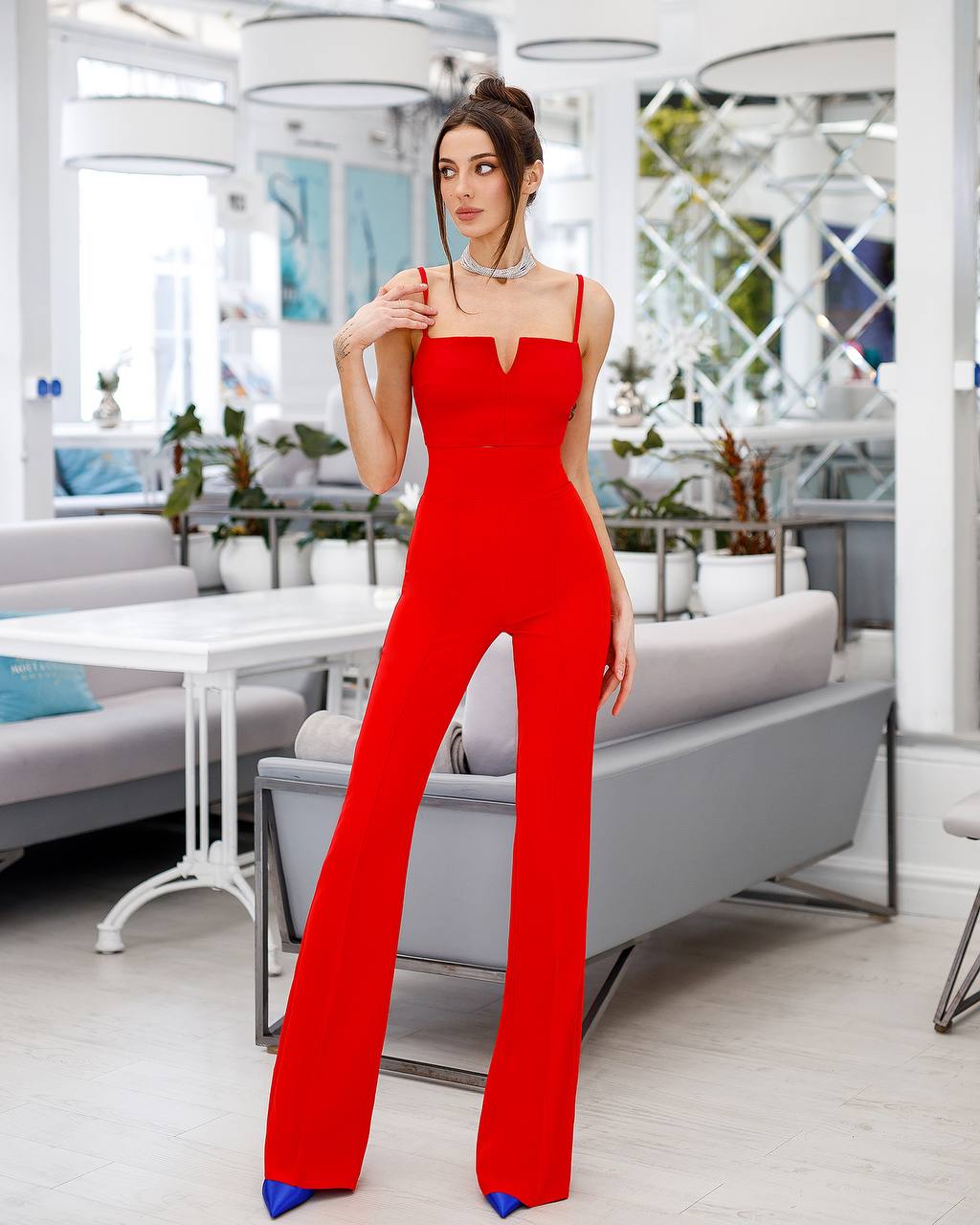 Woman in a red jumpsuit standing in a modern indoor setting with white furniture and plants.