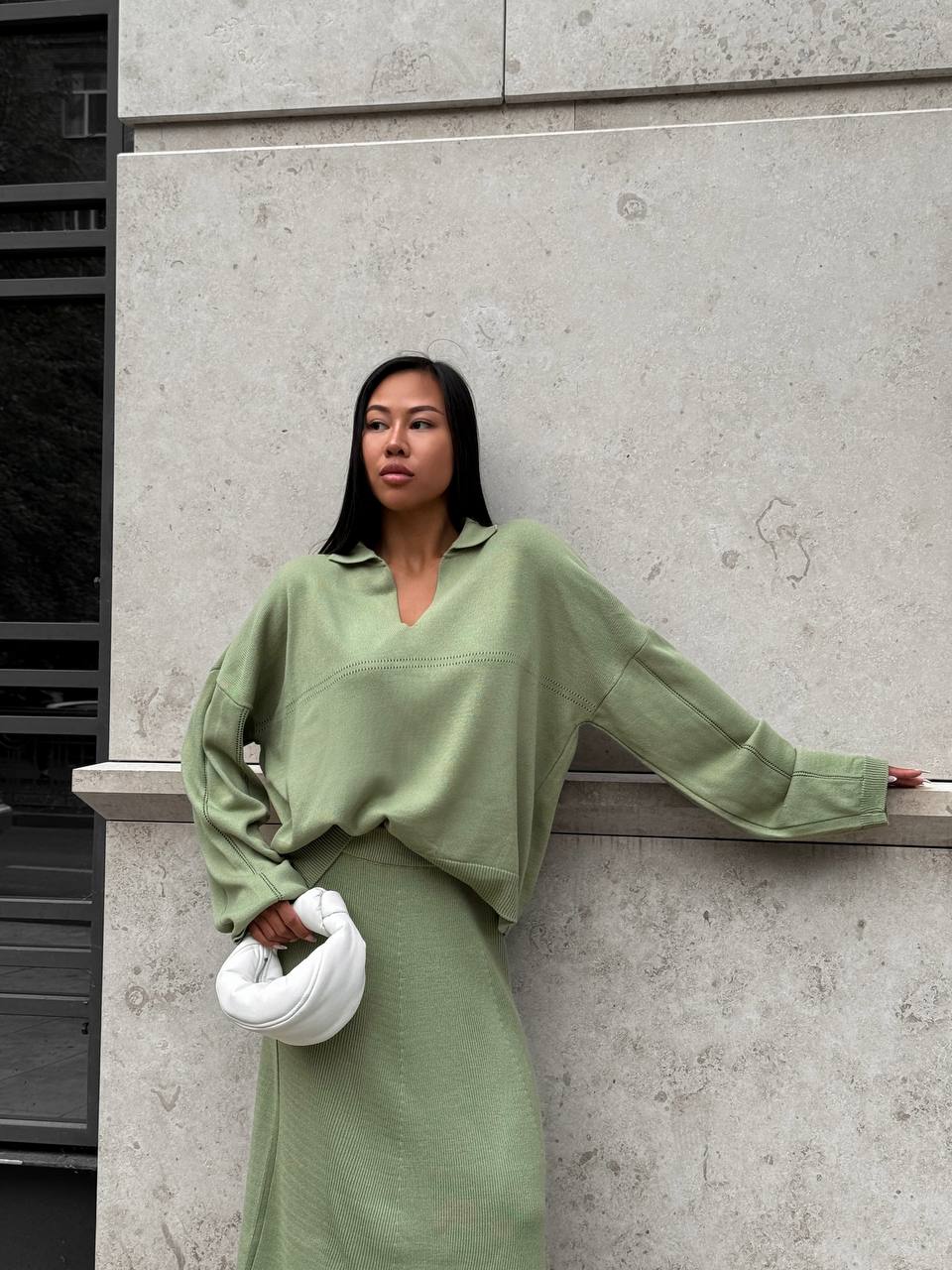 Woman in a green outfit leaning against a concrete wall.