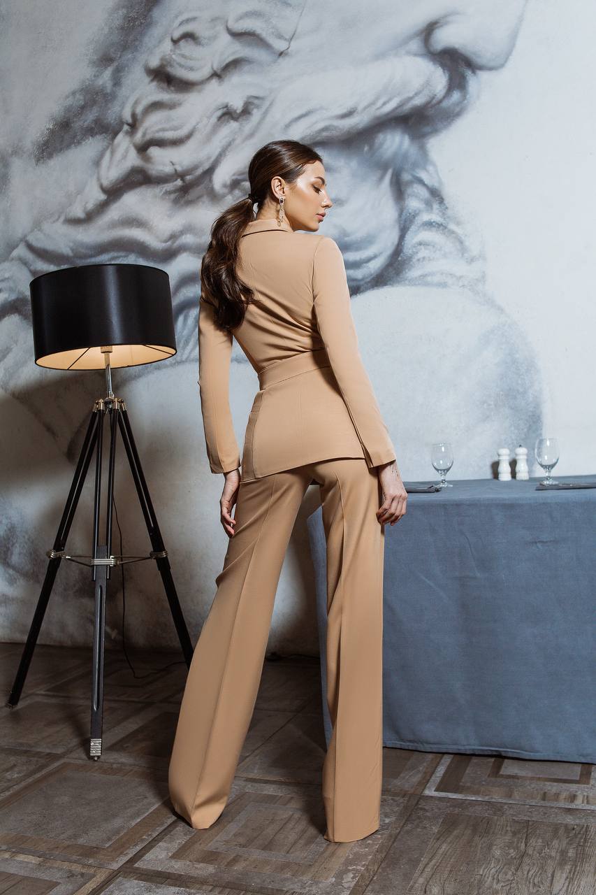 Woman in a beige outfit standing in a room with a lamp and sculpture in the background