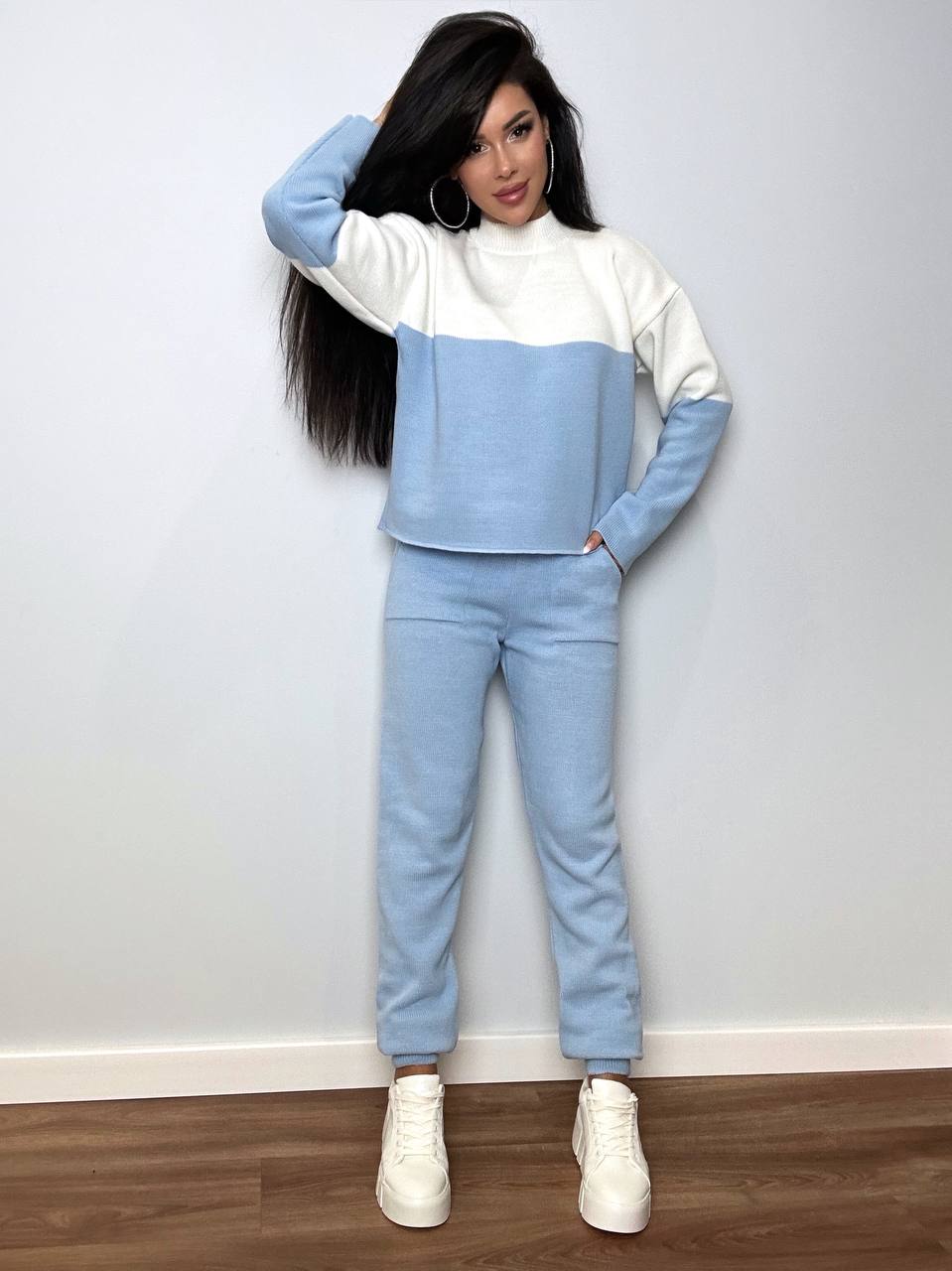 Person wearing a two-tone blue and white outfit with white sneakers against a plain background