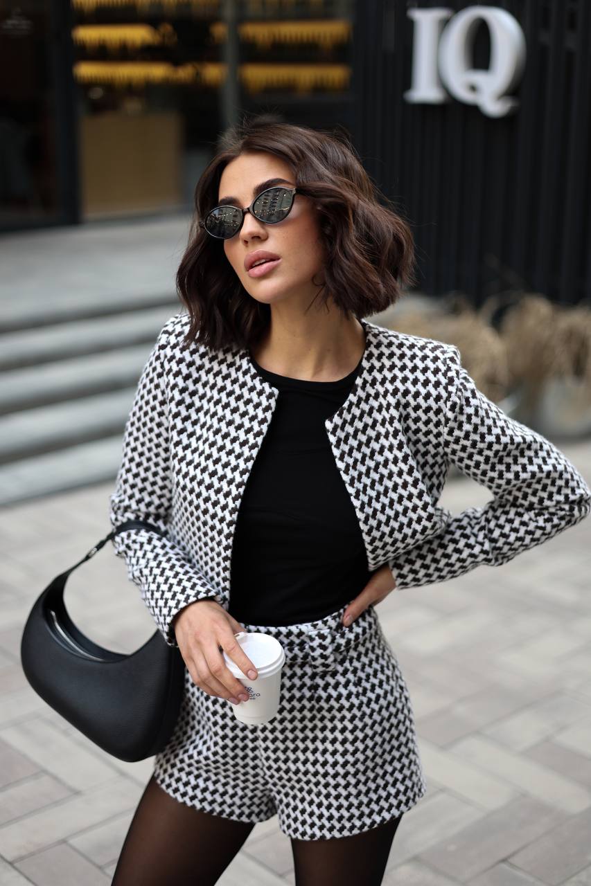Woman in a black and white checkered outfit standing on a street.
