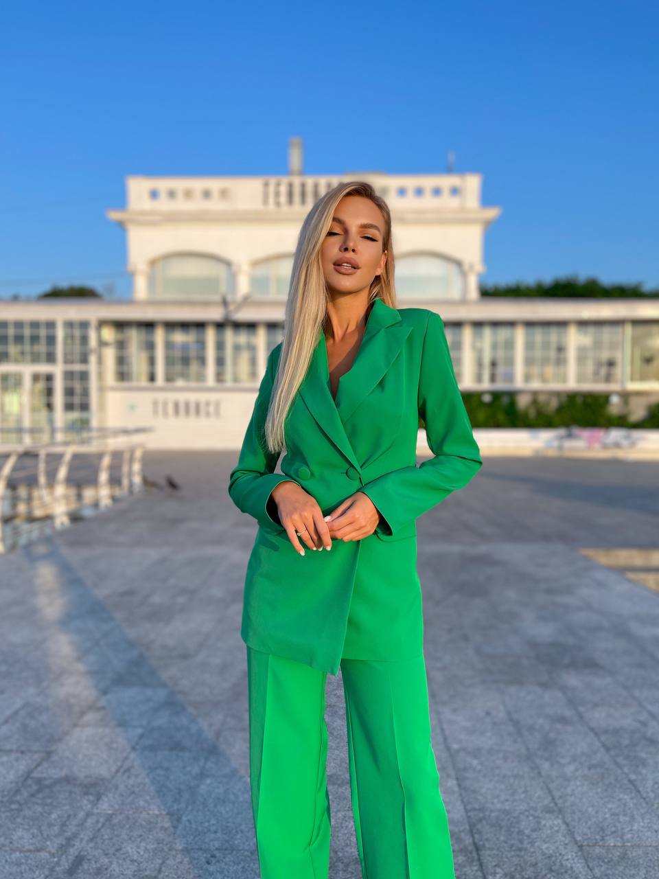 Woman in a green suit standing in front of a building with a blue sky.