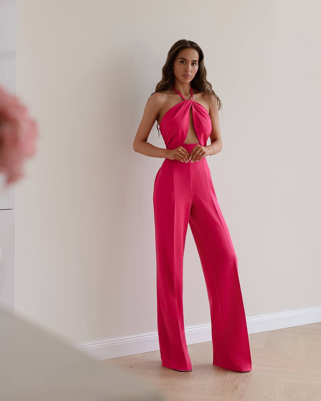 Woman wearing a bright pink jumpsuit against a plain wall.