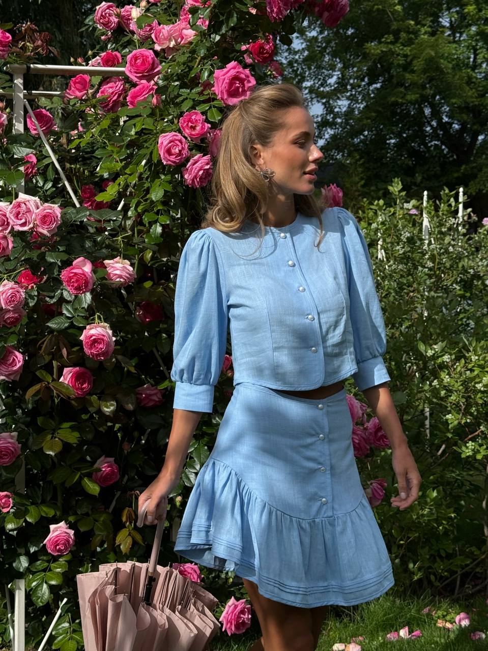 Woman in a blue outfit standing in front of pink flowers