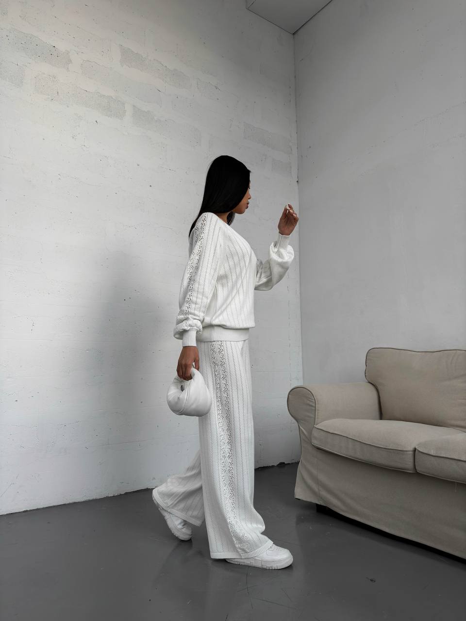 Person in a white outfit standing in a minimalistic room with a beige sofa.