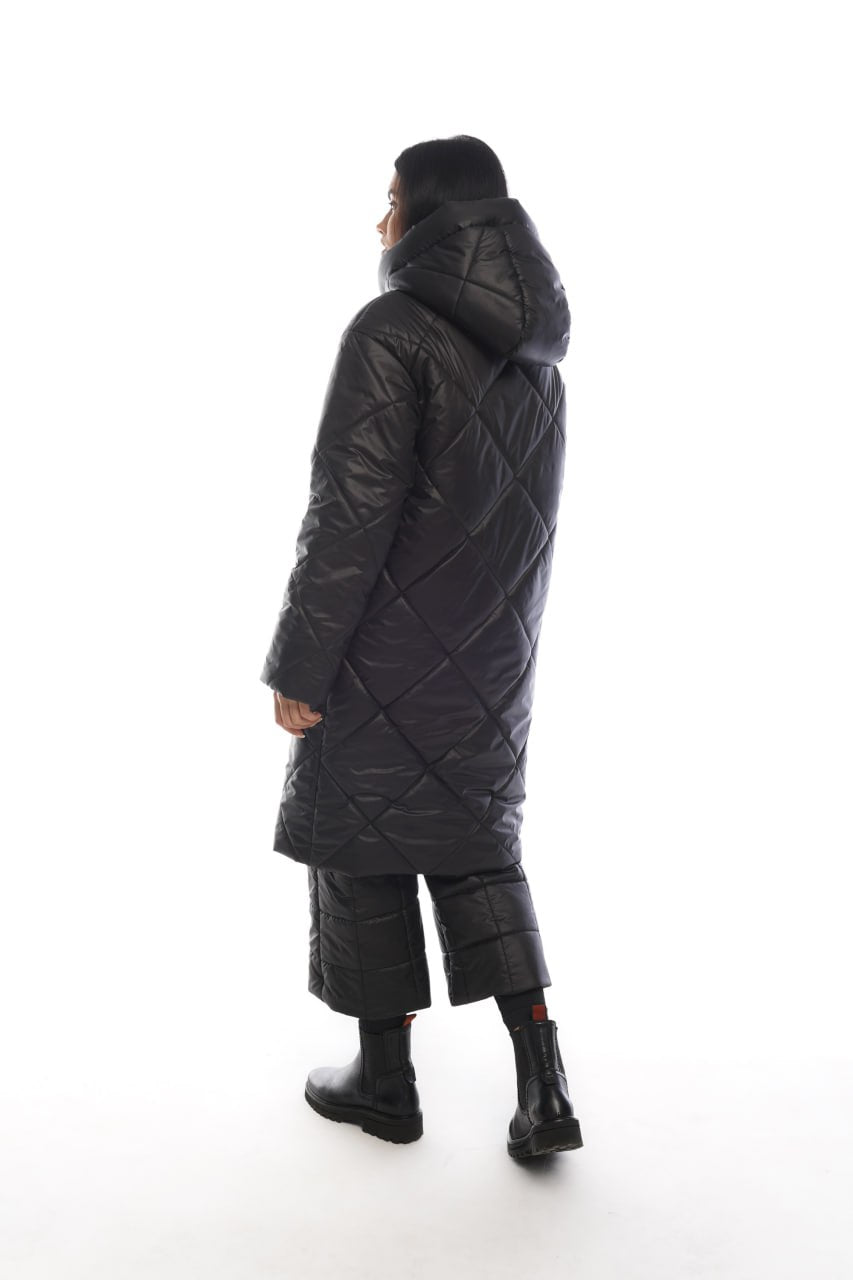 Person wearing a long black quilted coat on a white background