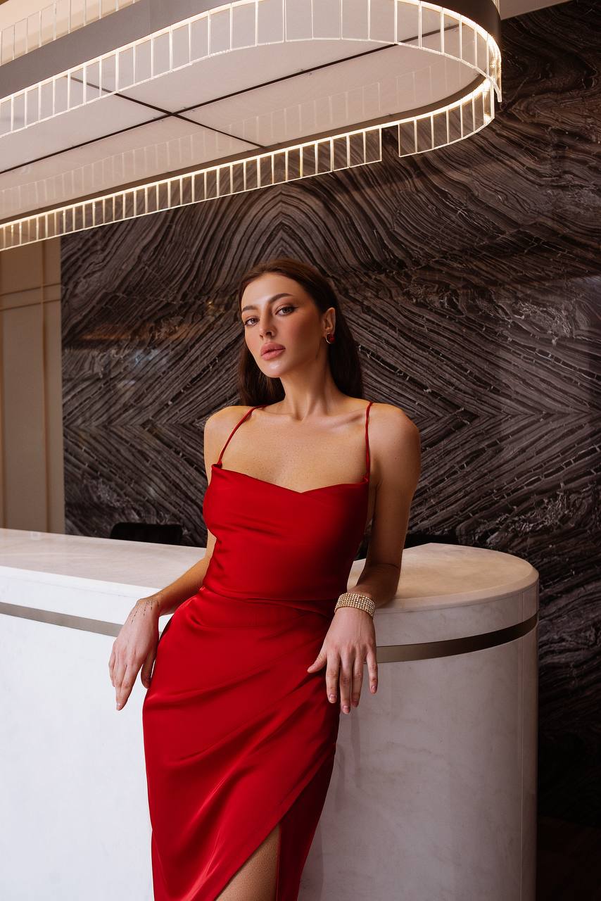 Woman in a red dress posing against a textured wall.