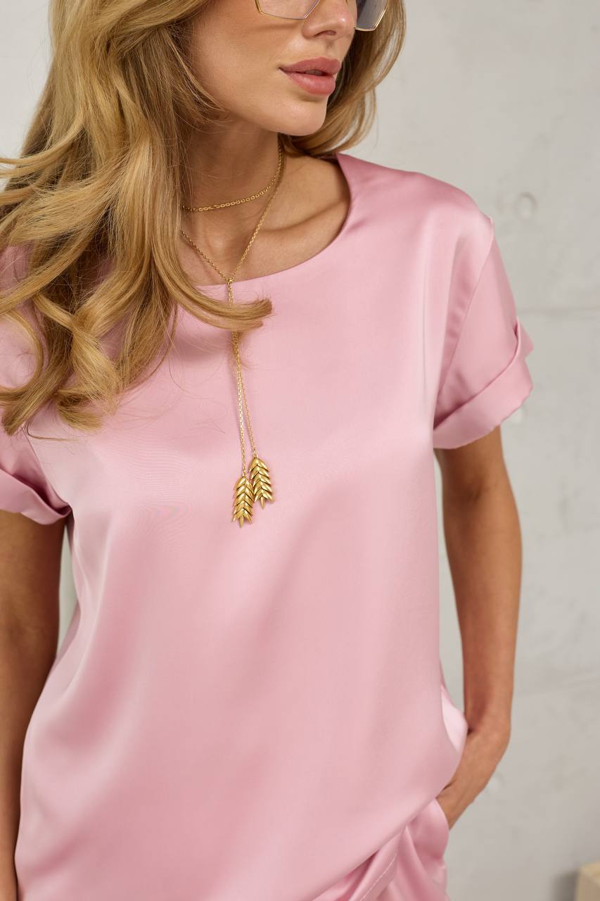 Woman wearing a pink satin dress with a gold necklace featuring an arrow pendant.