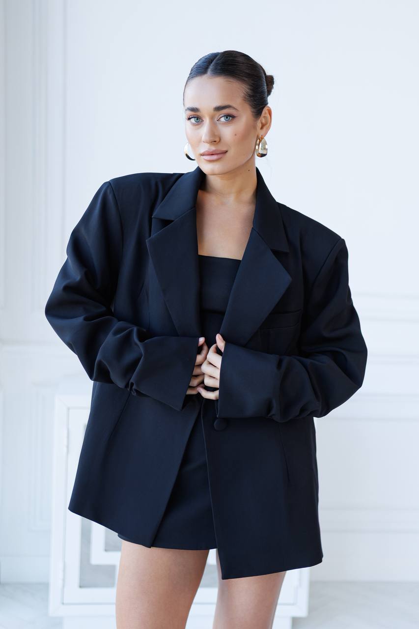 Woman wearing a black blazer and dress against a white background