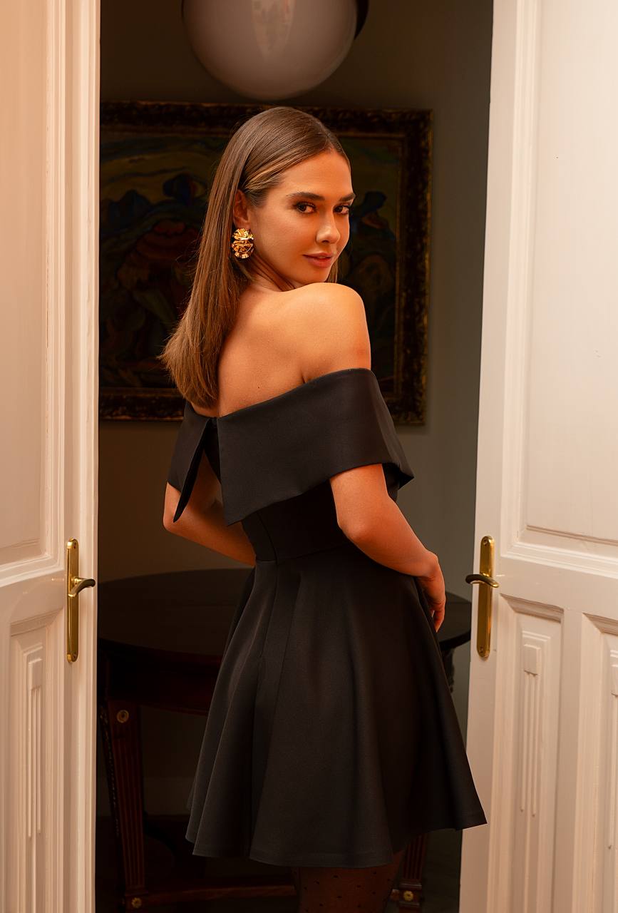 Woman in a black off-shoulder dress standing in a doorway.