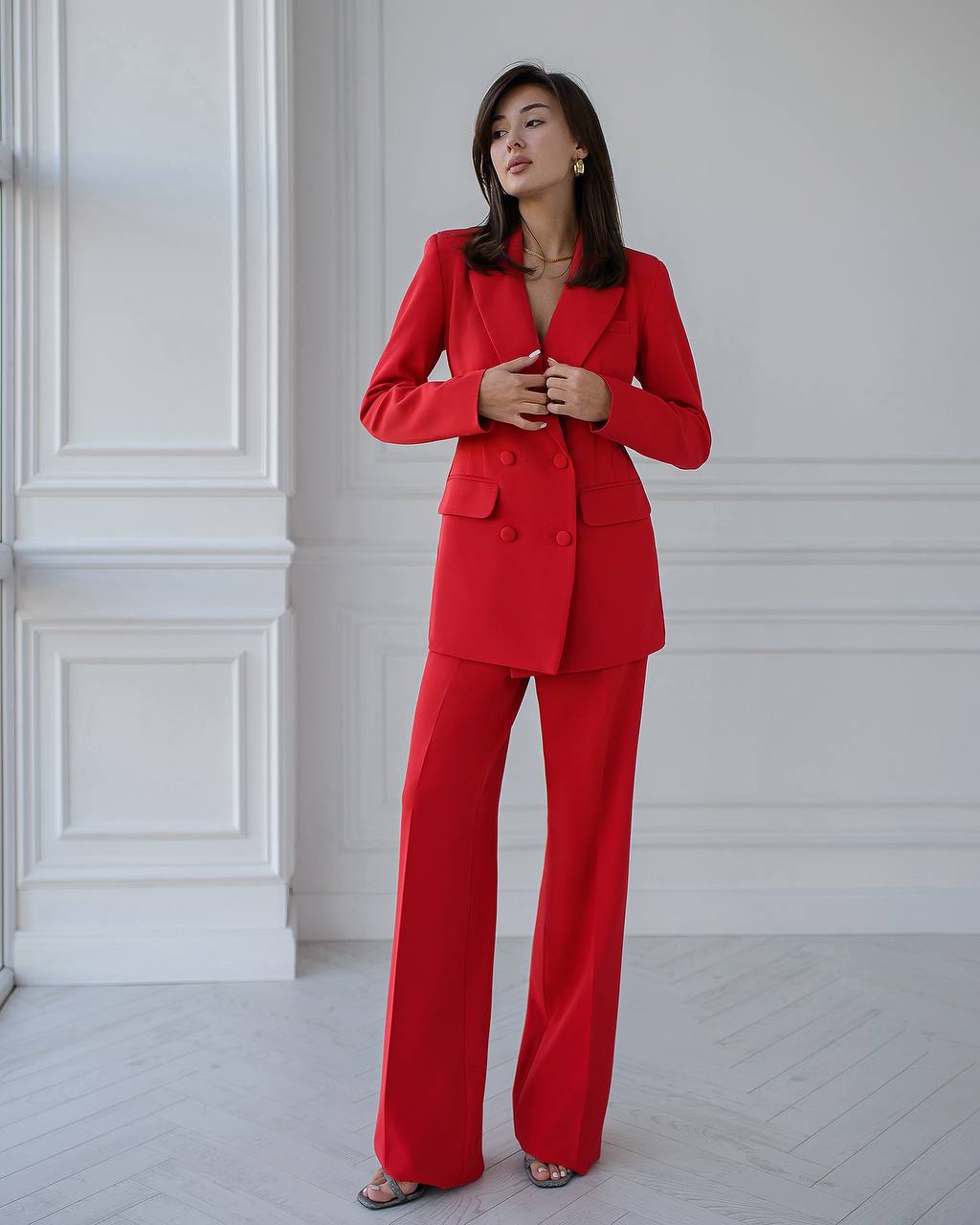 Woman wearing a red suit standing against a white wall.