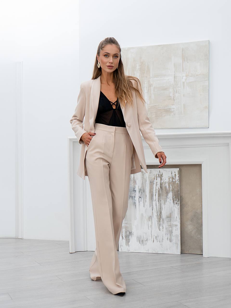 Woman in a beige suit standing in a modern interior setting with abstract art on the wall.