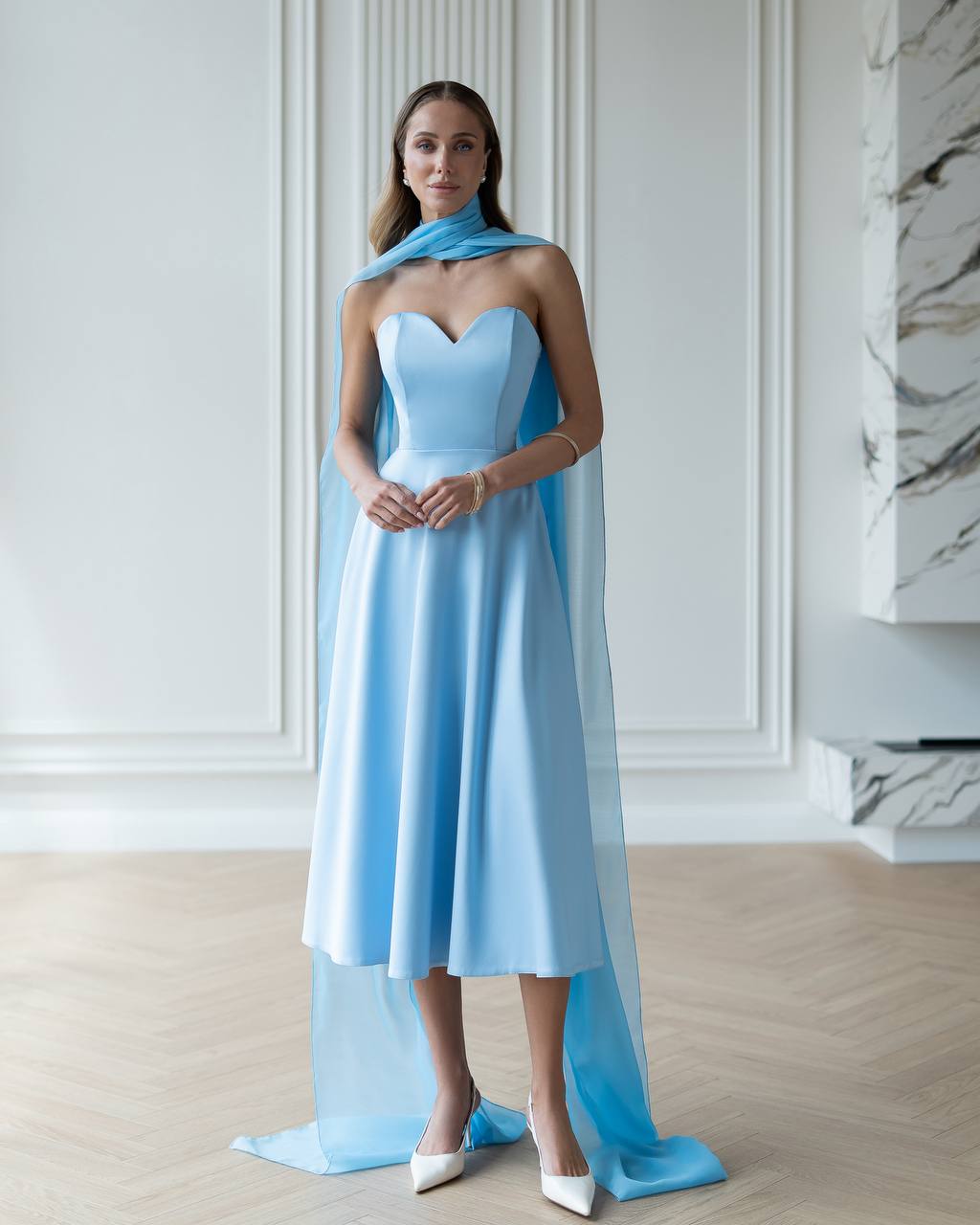 Woman wearing a light blue strapless dress with a matching scarf in an elegant room.