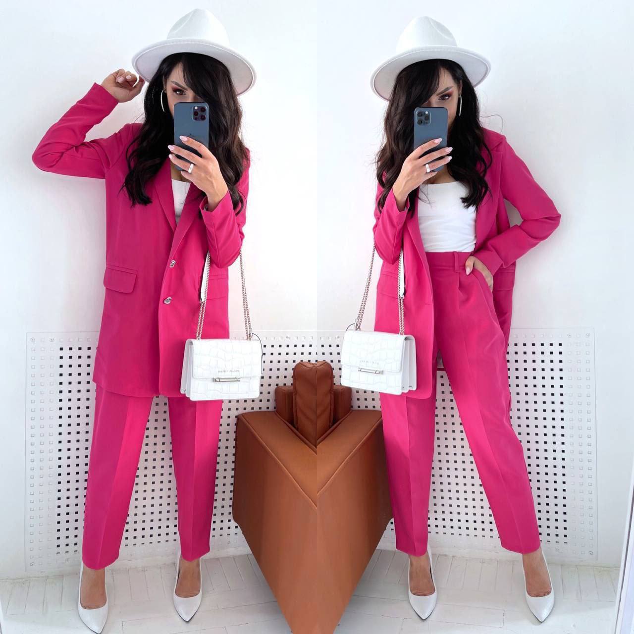 Woman in a pink suit taking a mirror selfie with a white hat and bag.