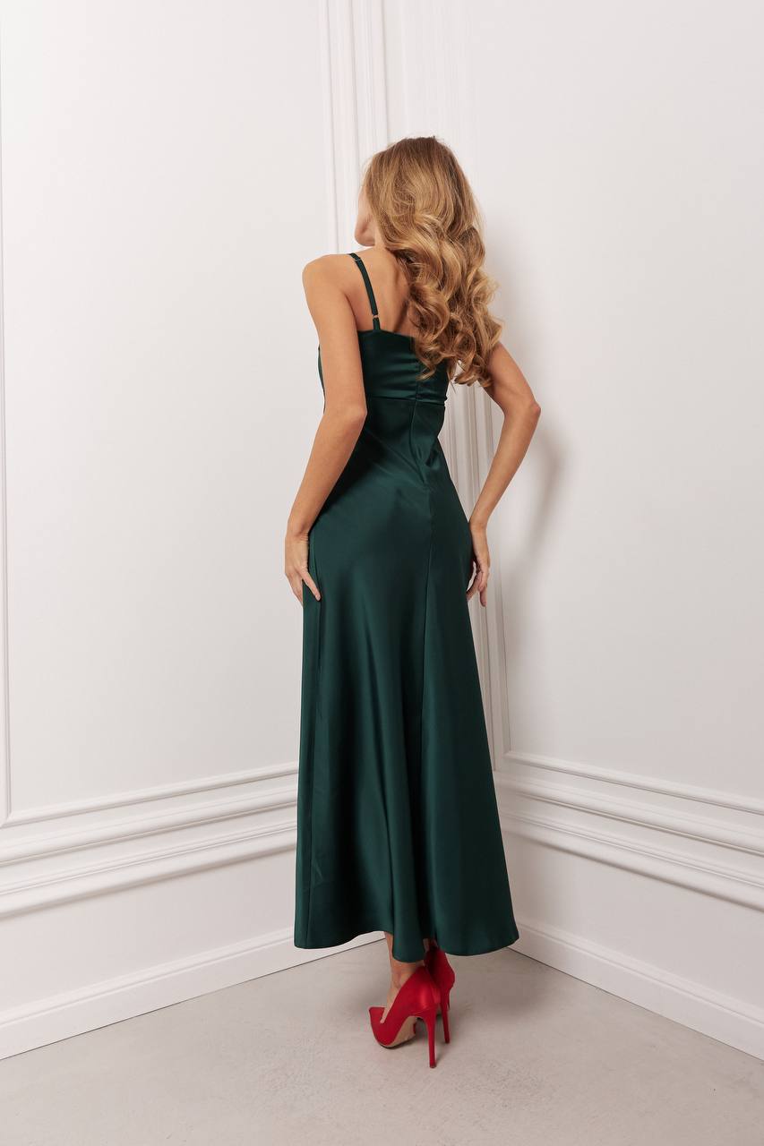 Woman in a long dark green dress with red high heels standing against a white wall.