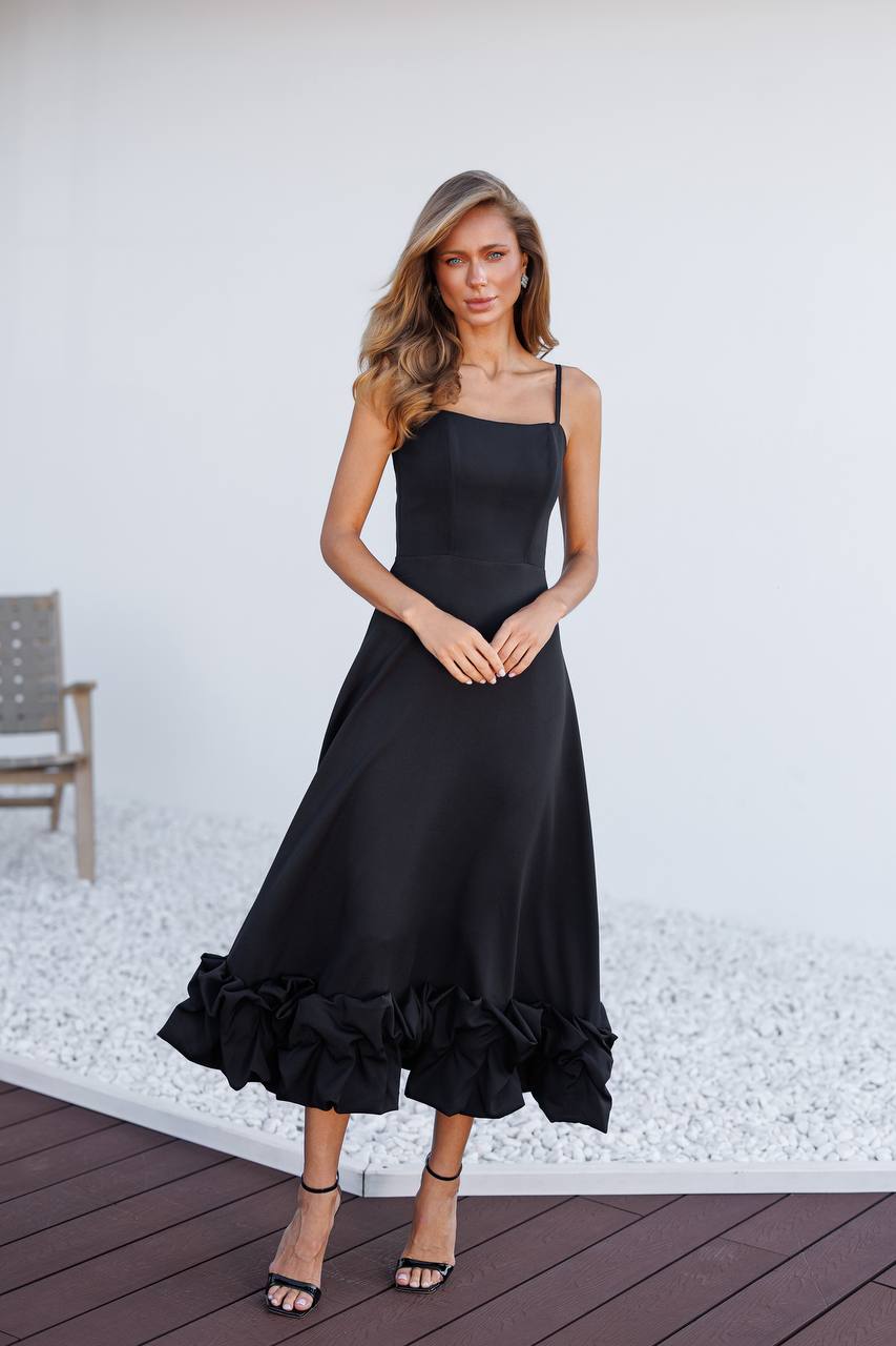 Woman wearing a black dress with ruffled hem on a wooden deck.