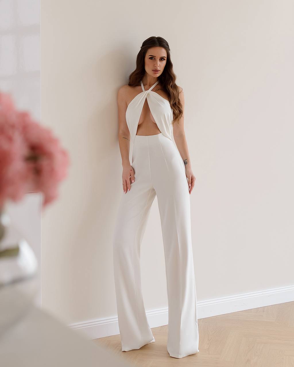 Woman wearing a white halter neck jumpsuit against a plain background