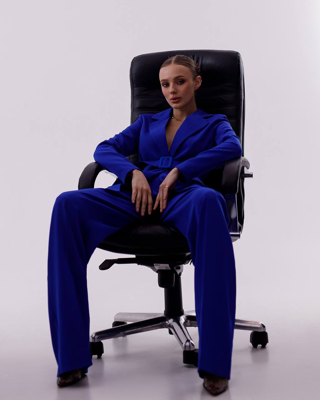 Person wearing a blue suit sitting on a black office chair against a white background