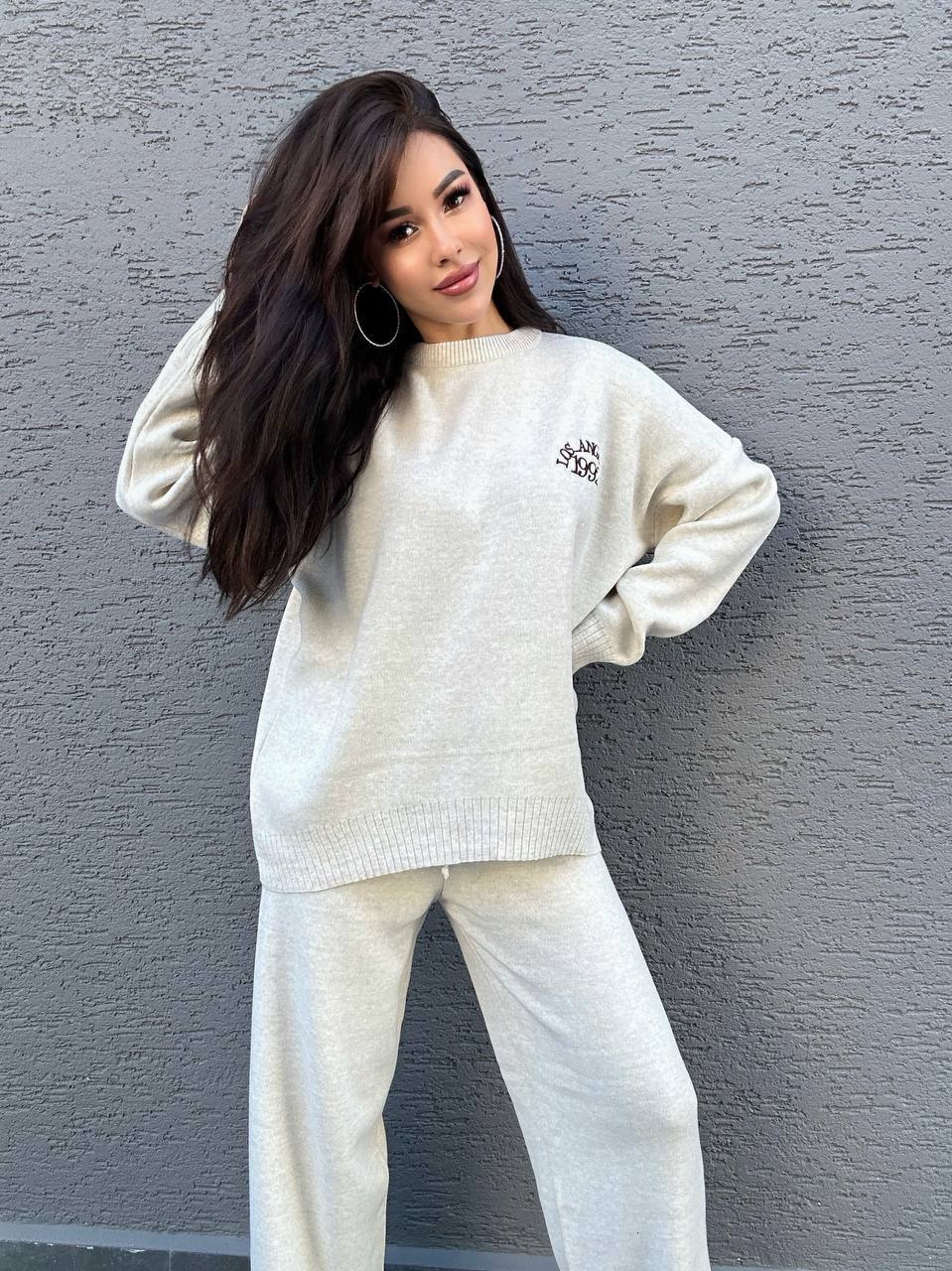 Woman wearing a white sweater and pants against a gray wall