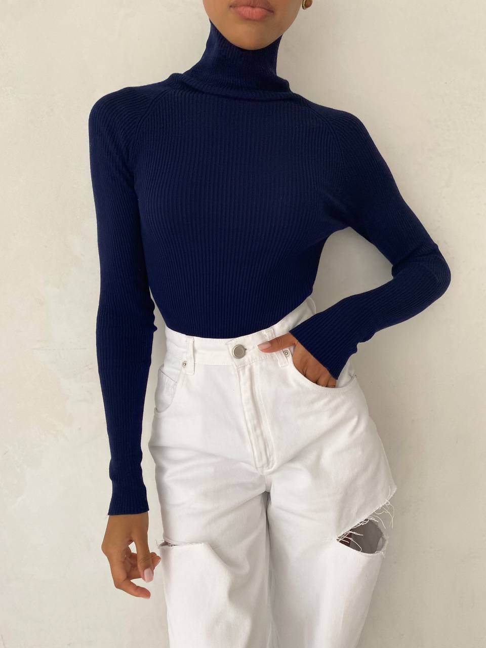 Person wearing a navy turtleneck and white pants against a plain background