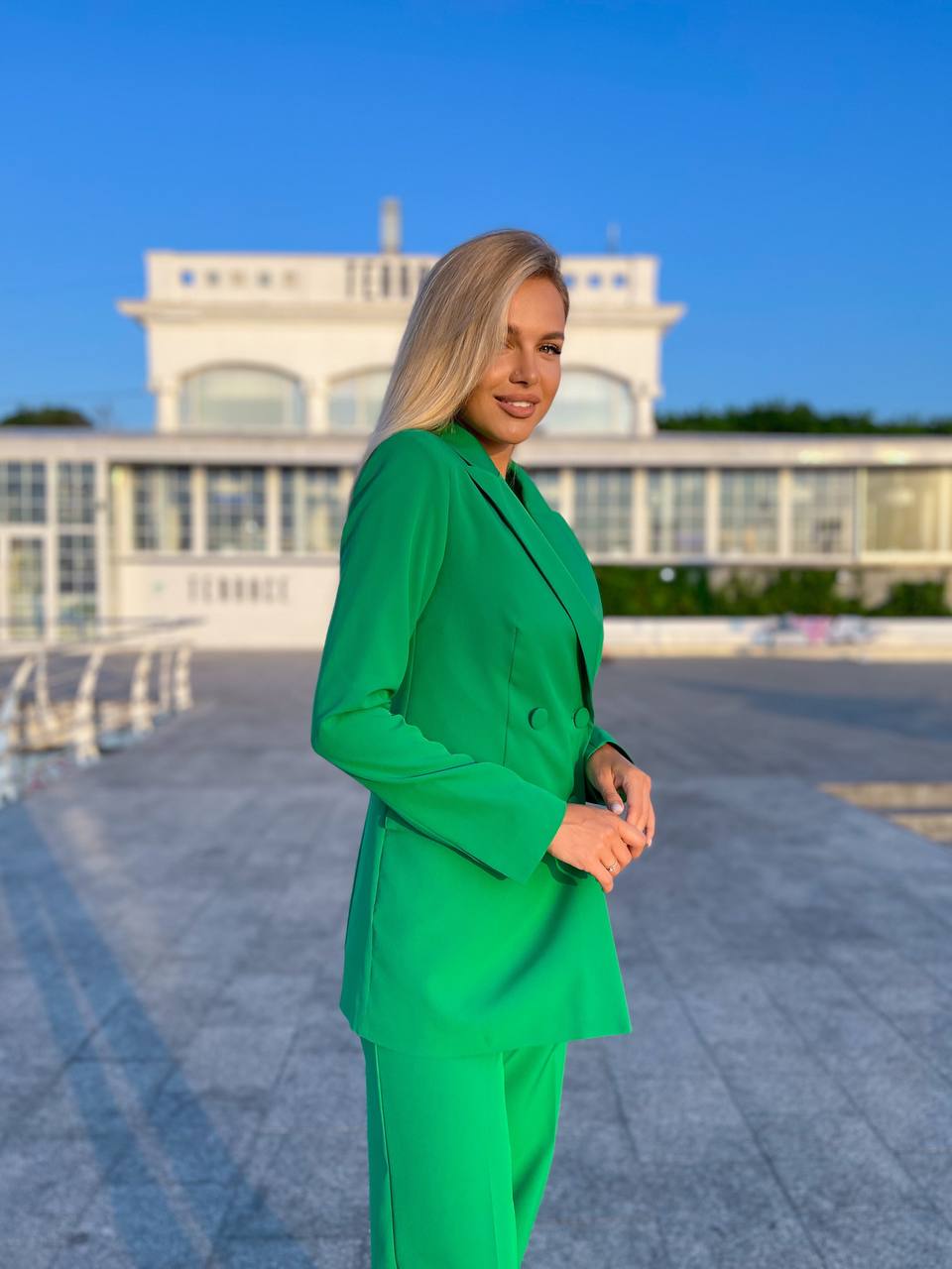 Woman in a green suit standing in front of a building with a blue sky.