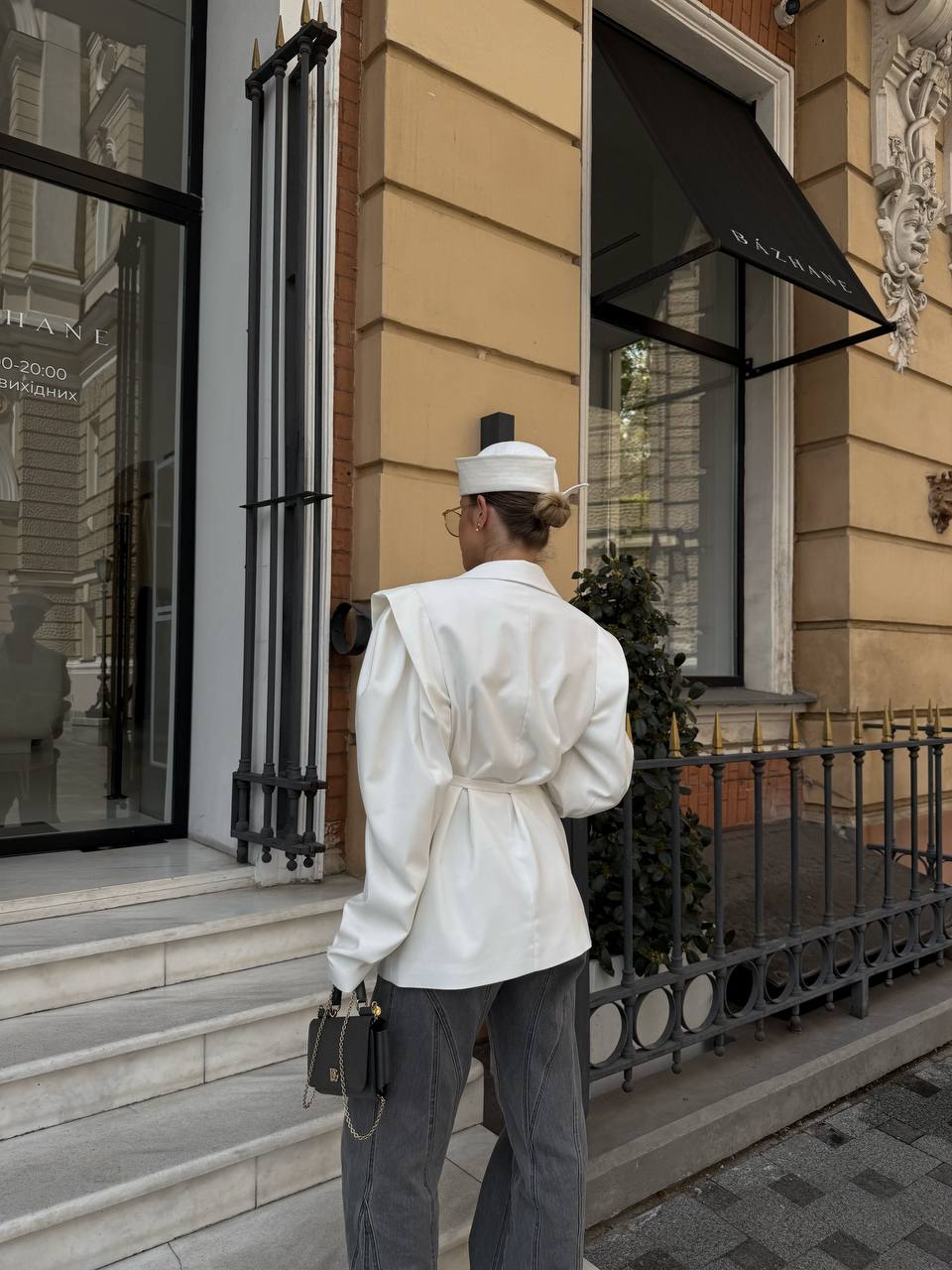 Person in a white outfit and hat standing on a city street in front of a building.