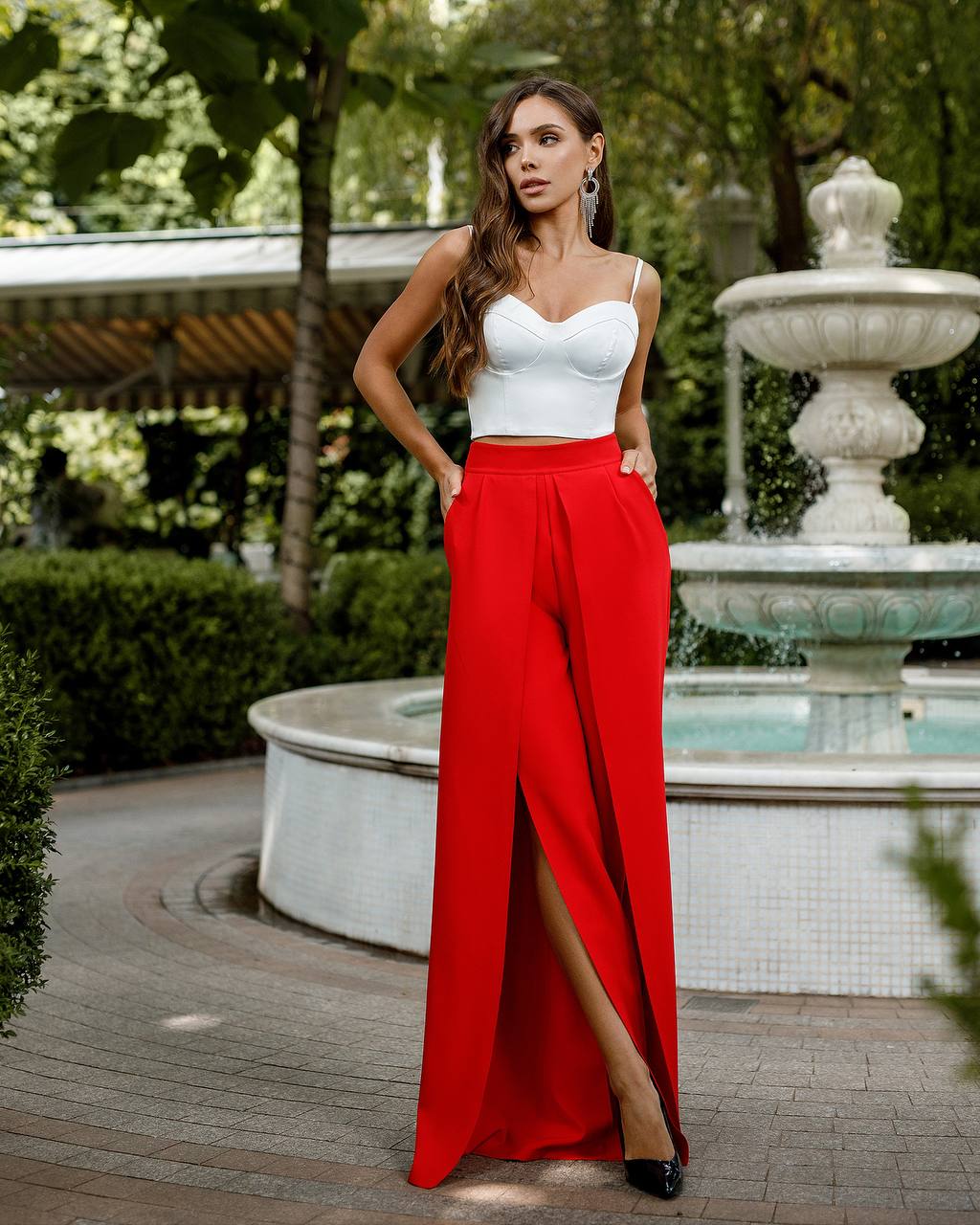 Woman in a white top and red pants standing in front of a fountain