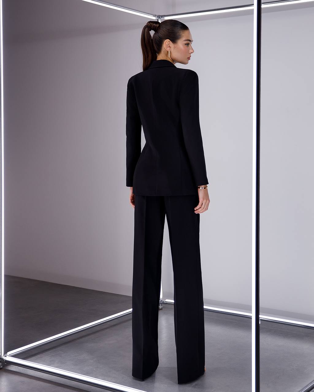 Woman wearing a black suit standing in front of a mirror.