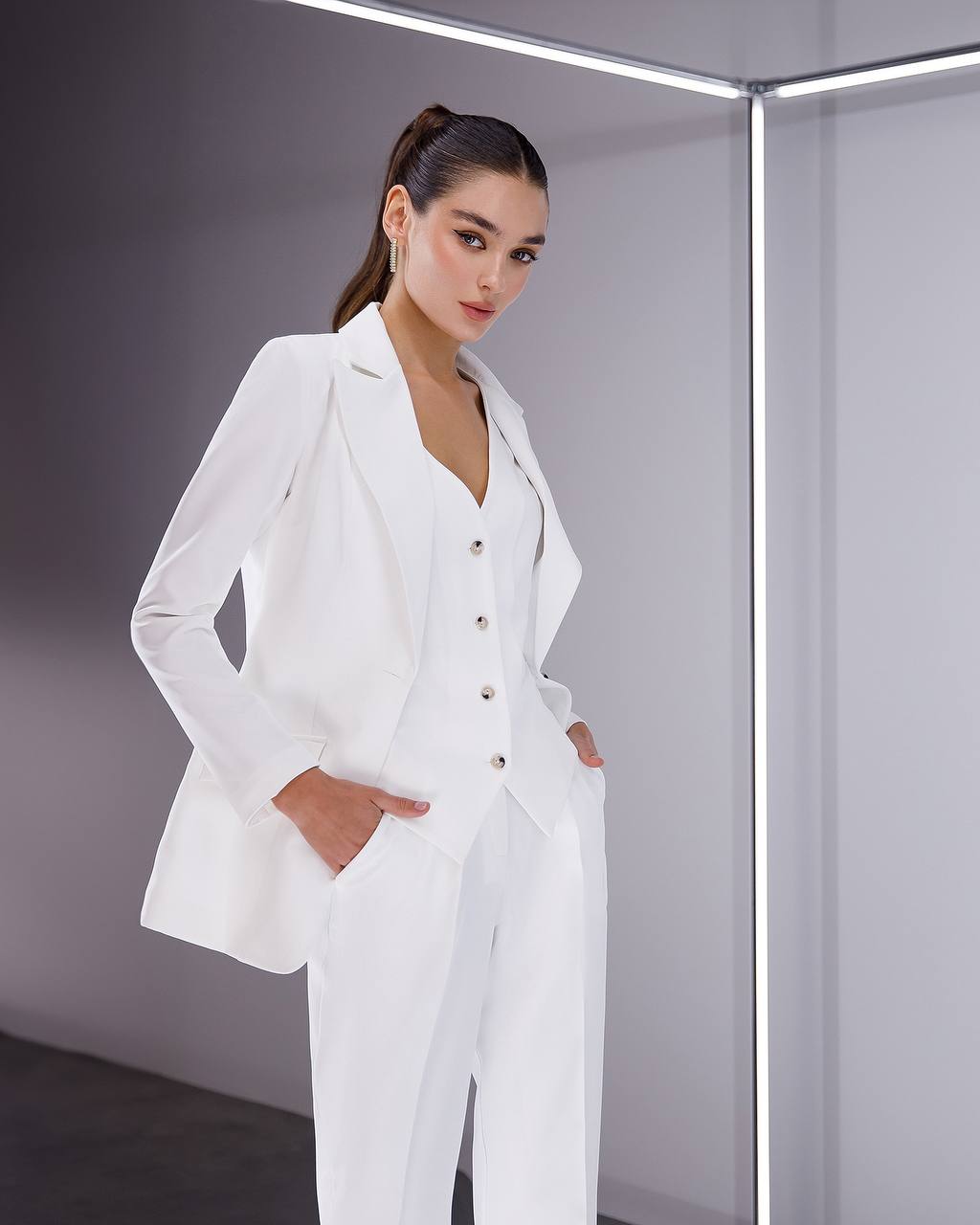 Woman wearing a white suit standing against a gray background