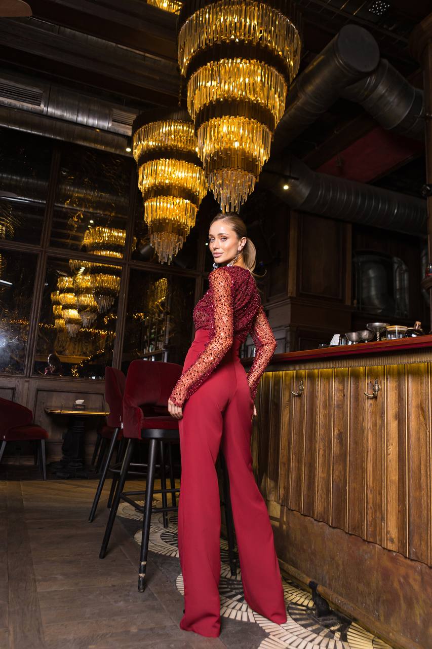 Woman in a red outfit standing in a bar with chandeliers hanging from the ceiling.