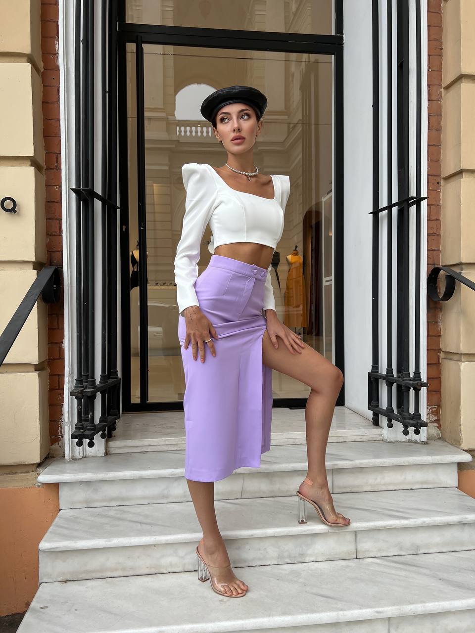 Woman in a white top and purple skirt standing on steps outside a building.