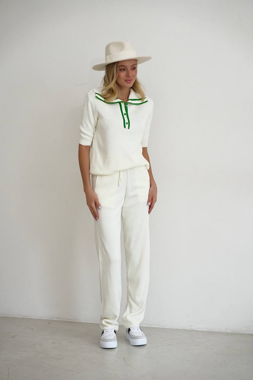 Person wearing a white outfit with green accents and a hat against a plain background