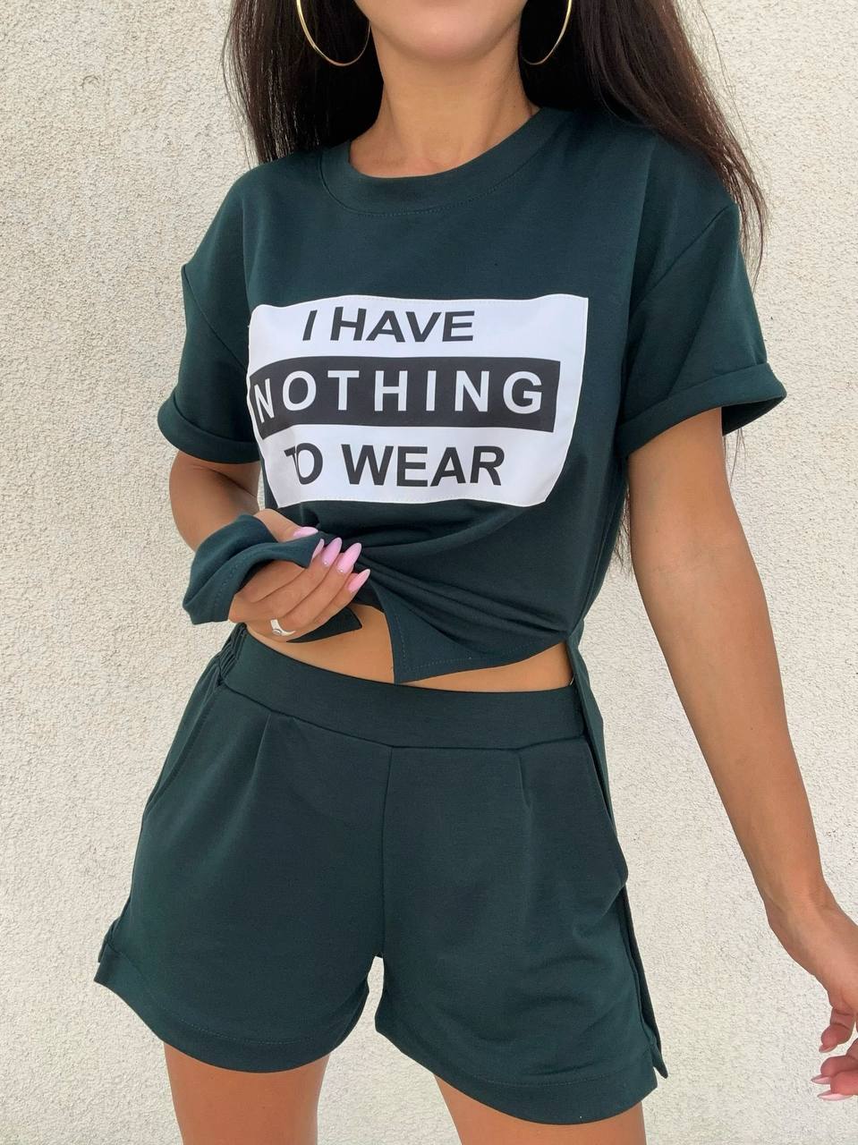 Person wearing a green t-shirt with 'I HAVE NOTHING TO WEAR' text and matching shorts on a neutral background