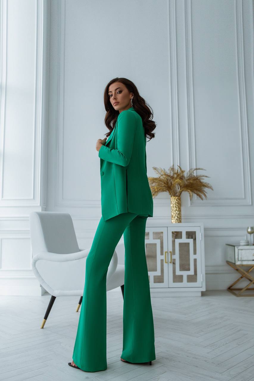 Woman in a green suit standing in a stylish room with white walls and decor.