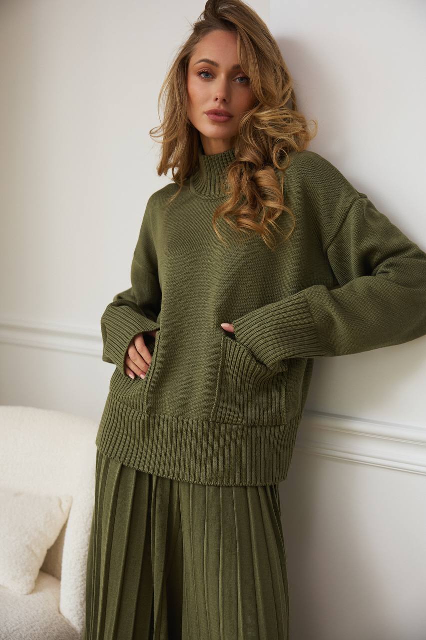 Woman wearing a green knit outfit against a white wall