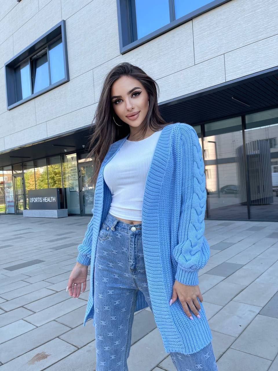 Woman wearing a light blue cardigan and jeans standing in front of a building.