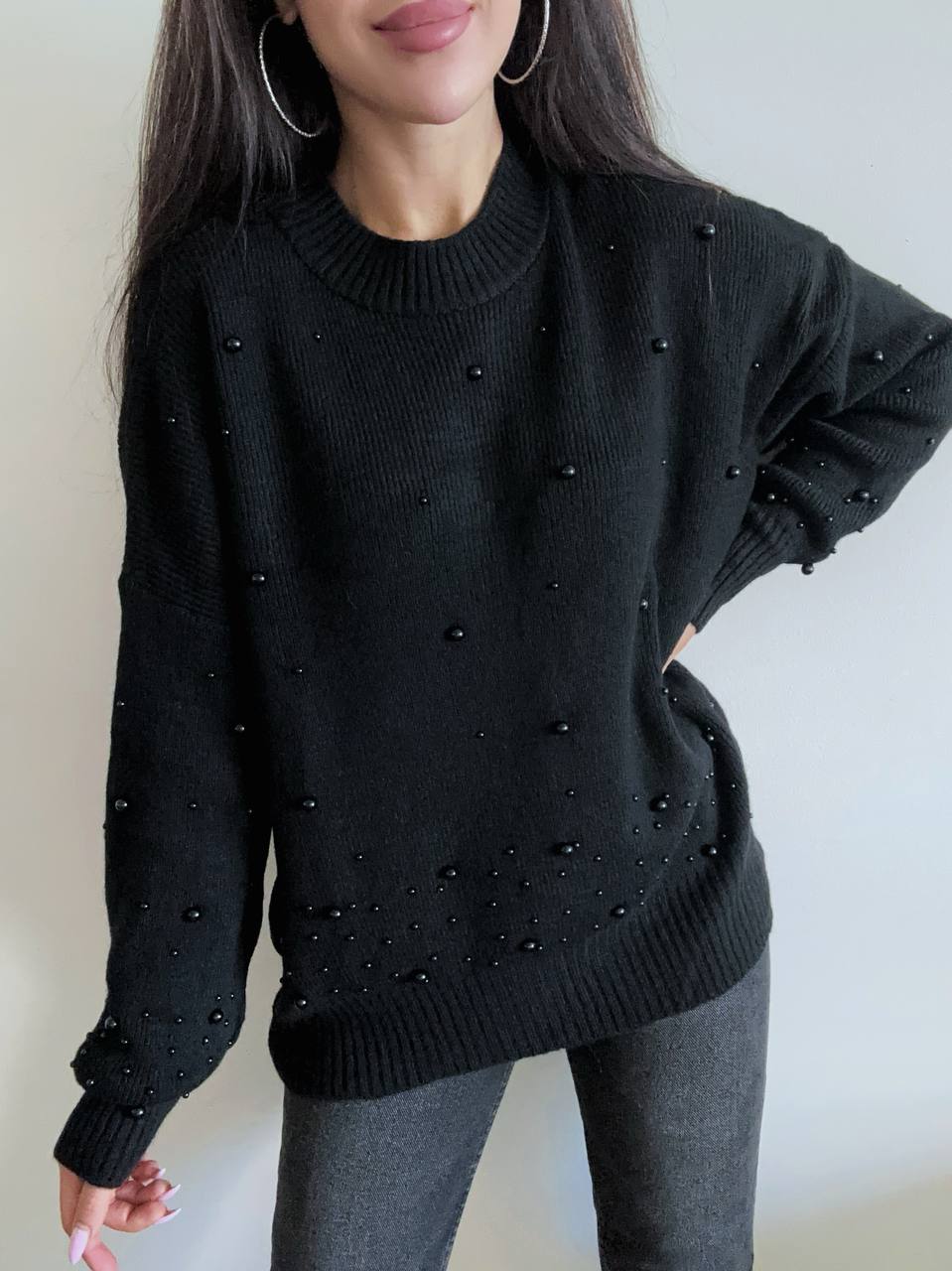 Person wearing a black sweater with bead embellishments against a neutral background