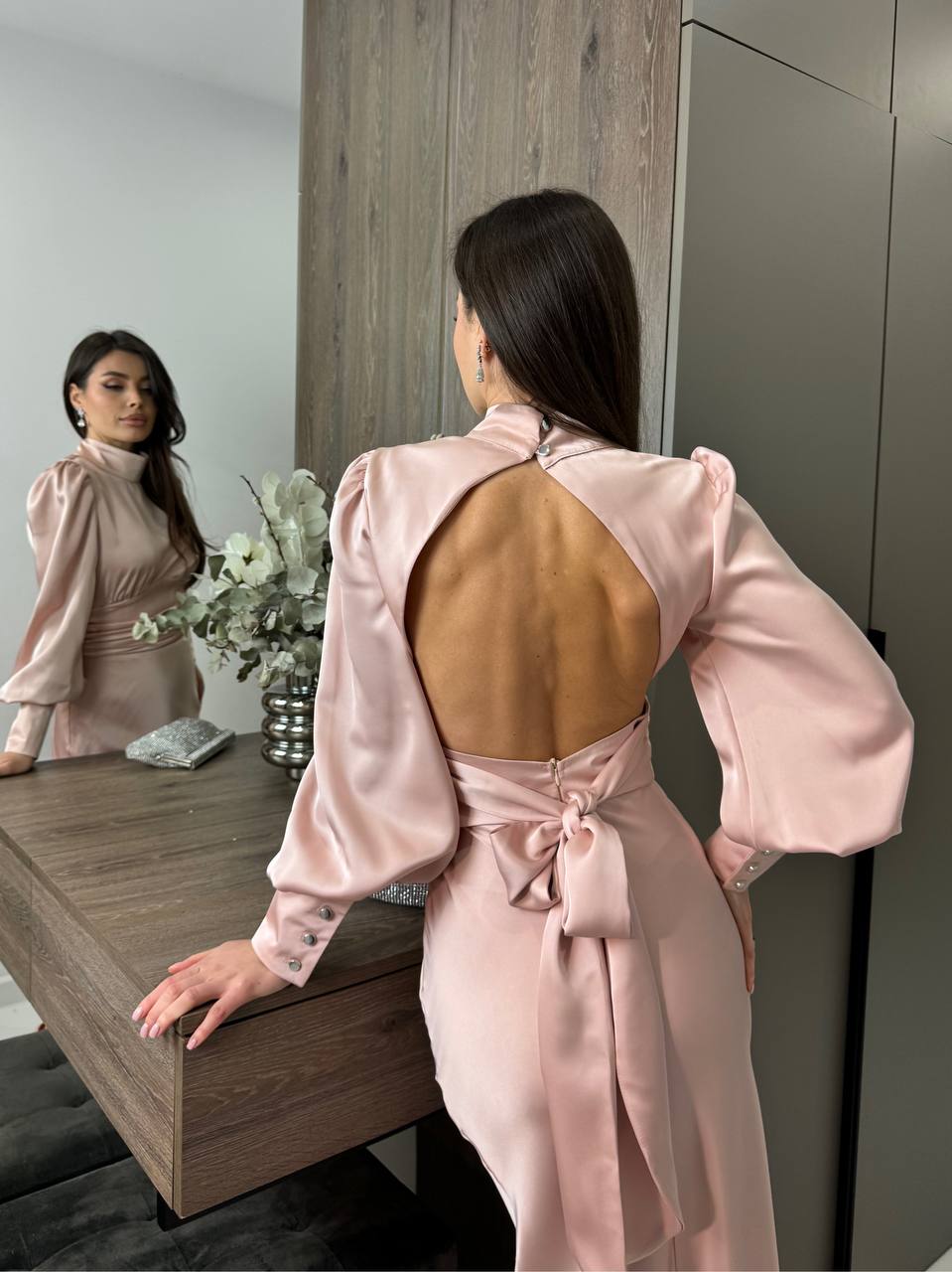 Woman in a pink dress with an open back standing in front of a mirror.